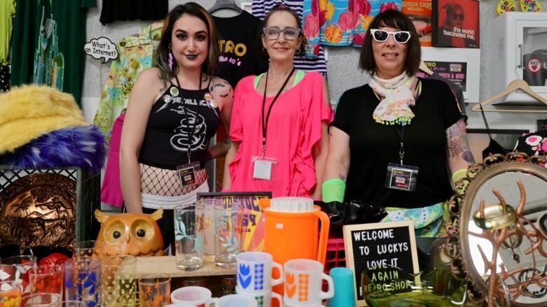 Three women pose behind a table filled with retro items.