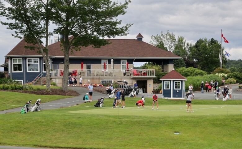 Several golfers practice their putting on a putting green in front of the club house. 