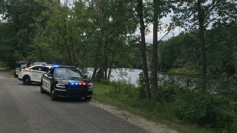 provincial police cars with their lights on parked beside a river.