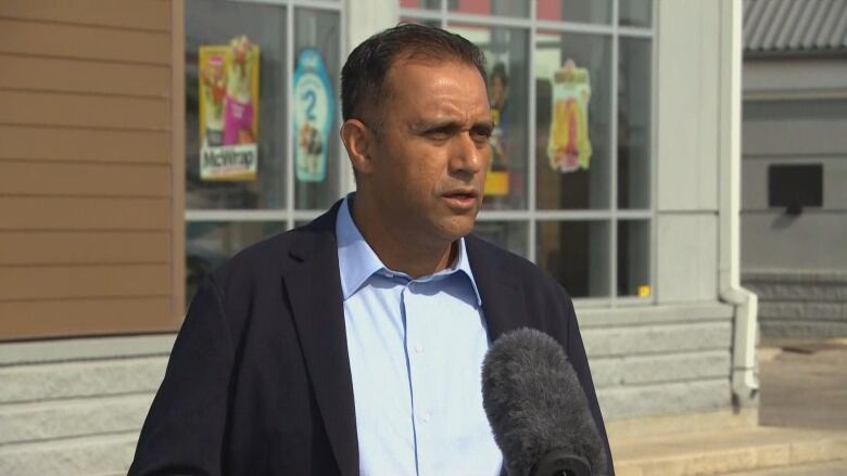 A man in a blue shirt and black blazer stands in front of McDonalds at a podium.