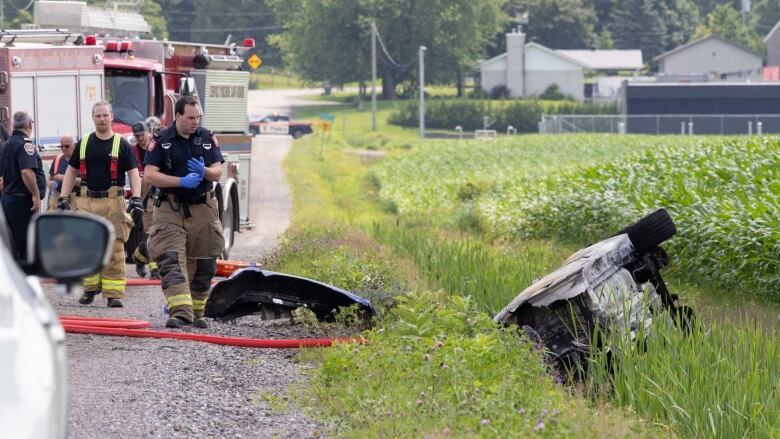 A car is flipped over in a ditch. First responders are on the scene. 