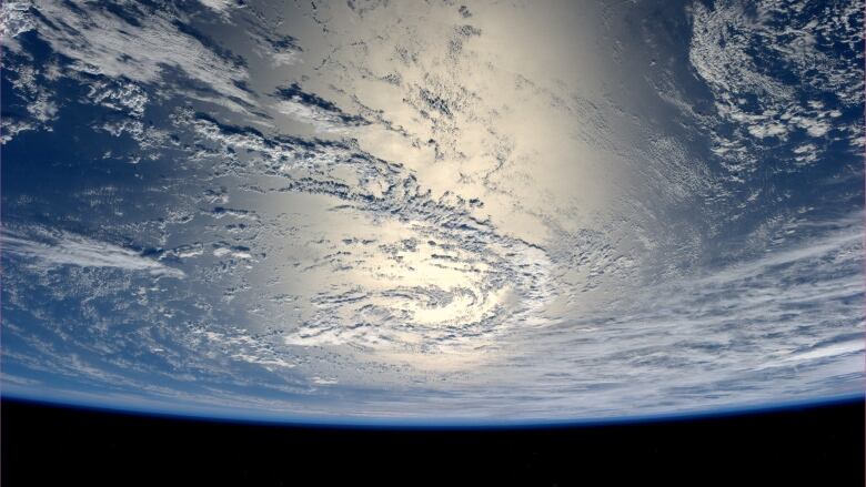 About one sixth of the Earth is visible in space. Clouds and blue are visible on the Earth, as well as a large area centred in the photo filled with glare.