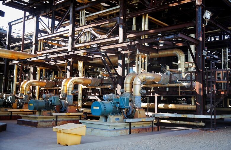 Pipes twist and turn through steel girders at an industrial site outside during the day.