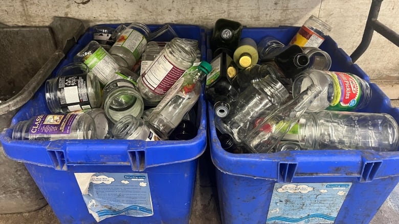 Two large bright blue bins are filled to the rim with glass bottles and jars. 