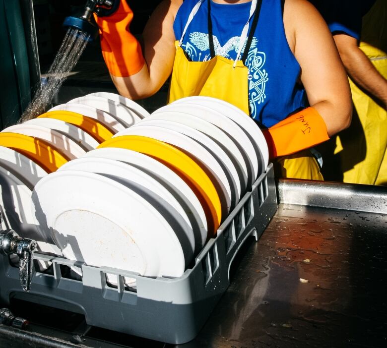 An unknown plate crew volunteer from the Edmonton Folk Festival washes a set of reusable melamine dishes for reuse. 