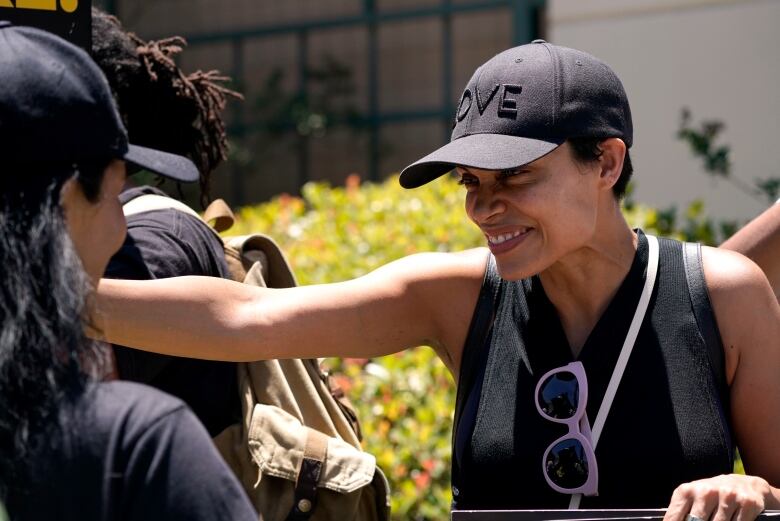 A woman smiles and rests her hand on the shoulder of another person while out on a picket line.