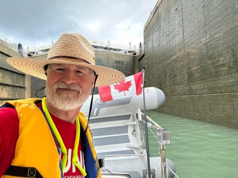 A man smiles at the camera as he travels by boat through a large canal