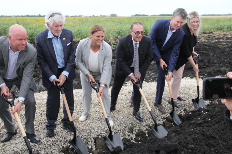 Several people pose for a photo at a ground-breaking with their shovel digging into the dirt.