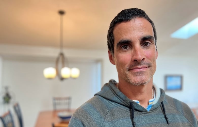 A man in a sweater stands inside of a home that is for sale.