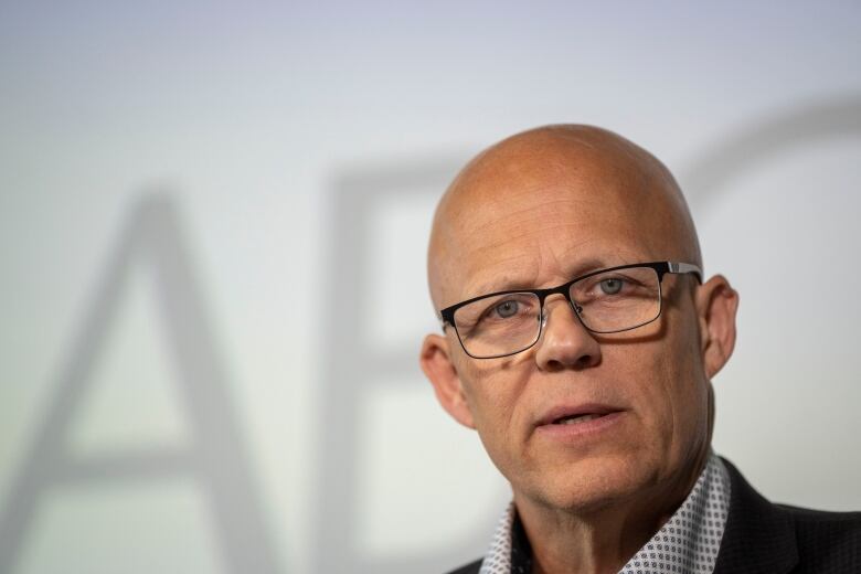 A bald white man looks at the camera with a white background behind him.