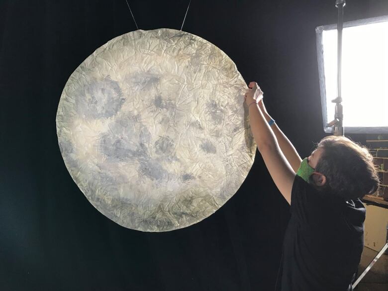 A set decorator hanging a paper moon.