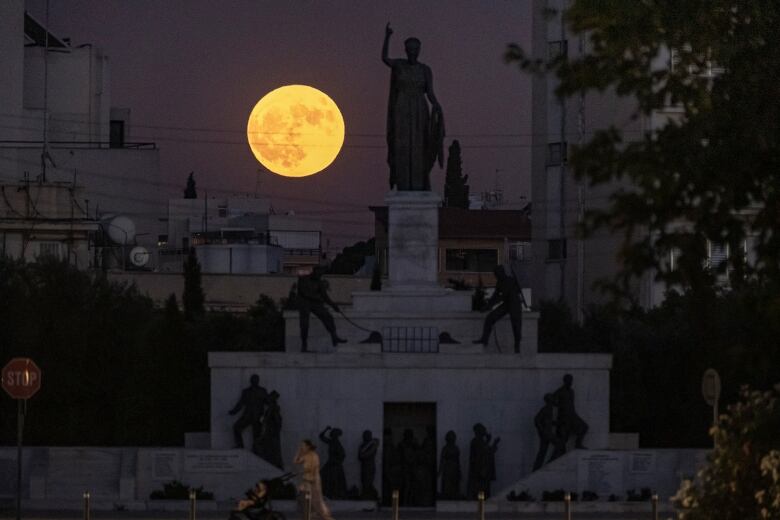 Full moon rising behind a group of statues.