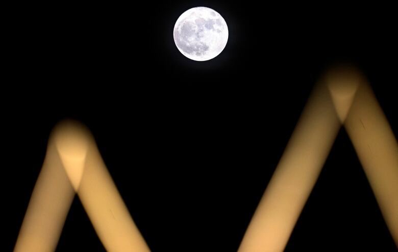 Lit structures of a sports complex in front of a full moon.