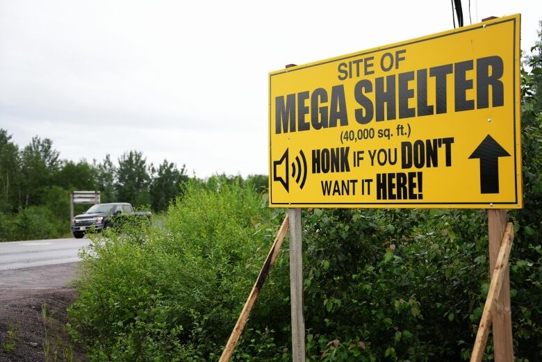 A sign reads 'Site of mega shelter, 40,000 square feet. Honk if you don't want it here!' 