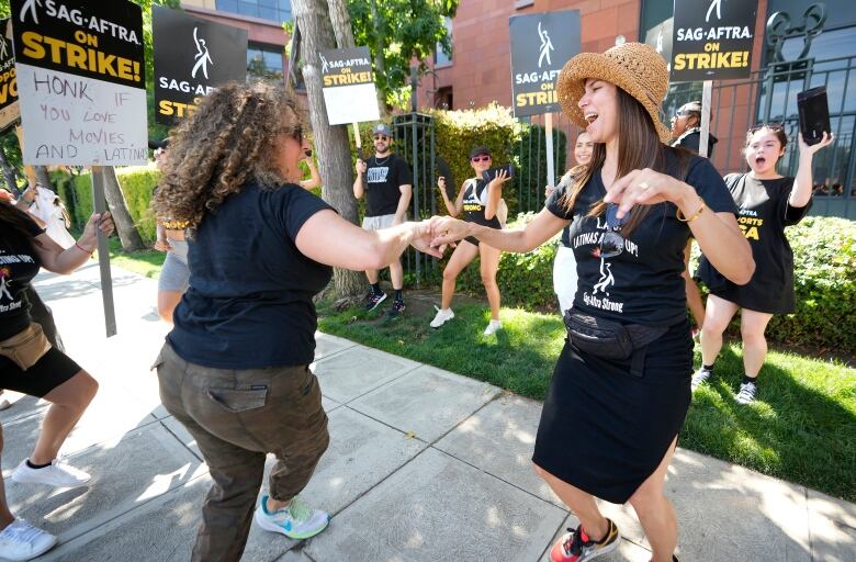 Two women in the foreground clasp hands with one another, while onlookers surround them on a picket line outside Disney studios in Burbank, Calif.