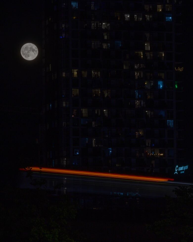 A large moon is seen next to a high rise apartment tower.