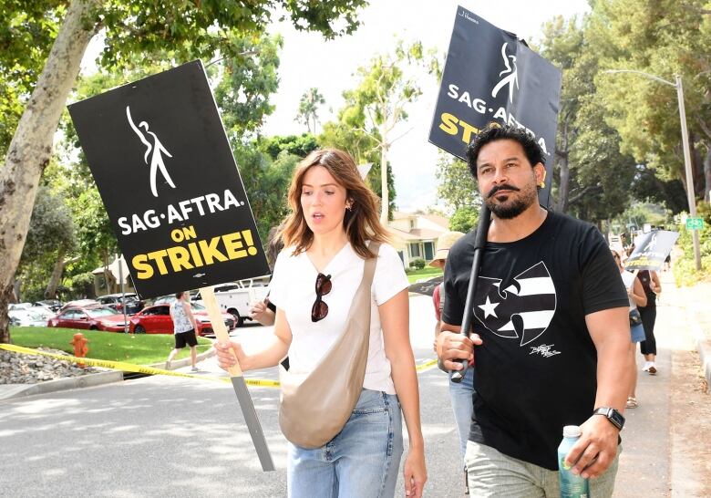 A man and woman holding signs, picketing outside a Walt Disney Studios in Burbank, Calif.