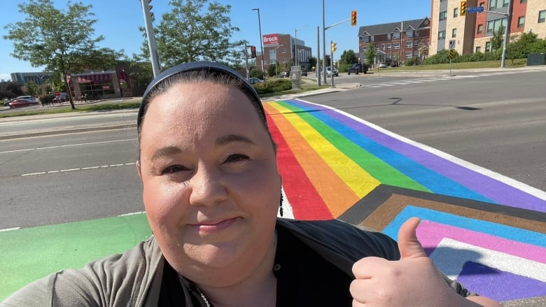 A woman wearing a headband smiles in front of a progress pride flag crosswalk.