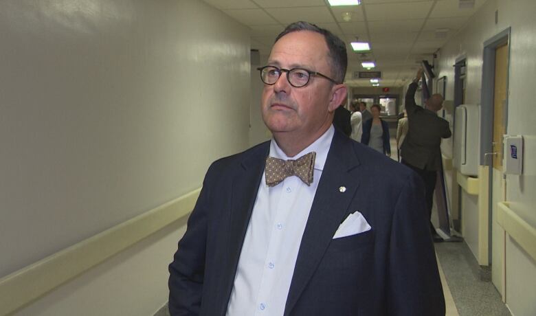 A man in glasses and a bowtie stands in a hospital hallway.