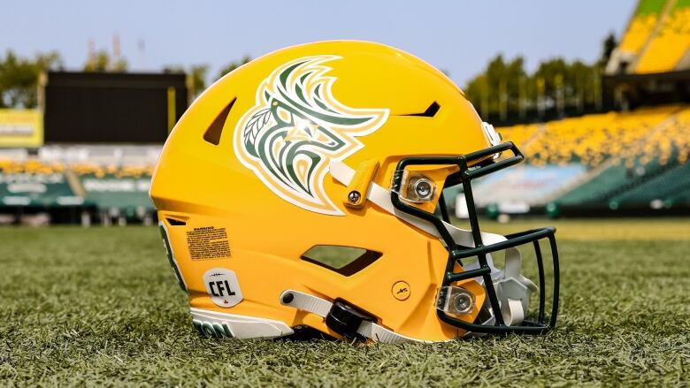 A football helmet sits on a field in an empty stadium during a summer day.