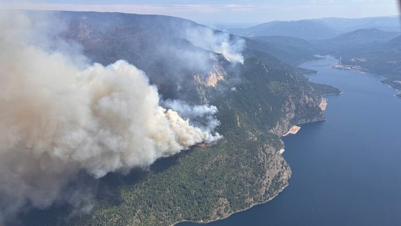 Plumes of smoke rise from a lakeside hilltop.