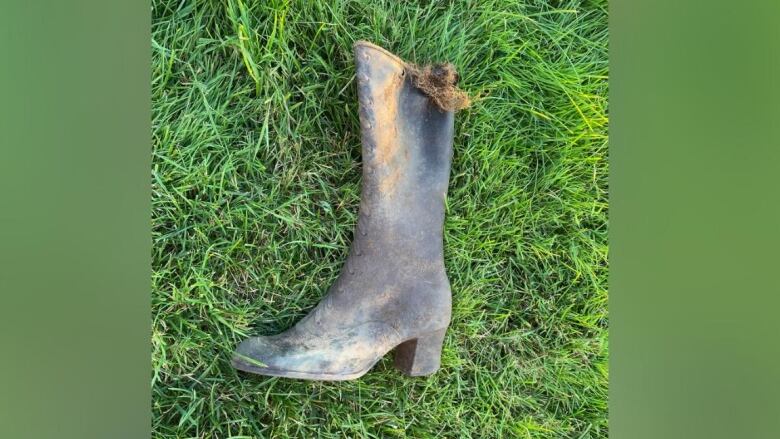 An old, black, high-heeled rubber boot lays on its side on a grassy lawn.