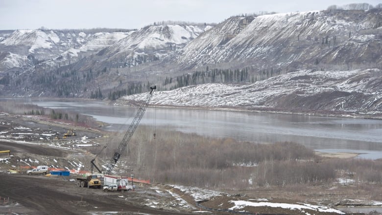 A wide shot of a river with mountains in the background and a truck sitting on the river bank.