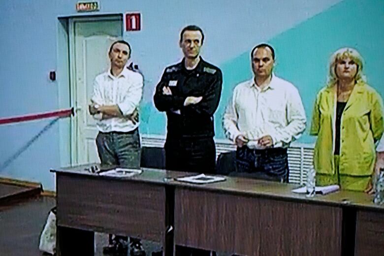 Three men and a woman appear on a video screen during a court hearing in Russia.