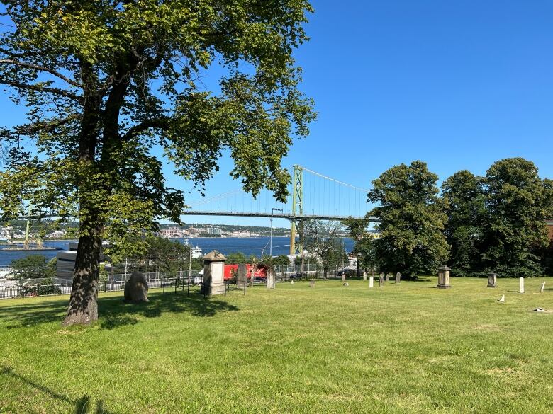 A view of a cemetery with a few grave markers and Halifax Harbour and the Macdonald bridge in the background.