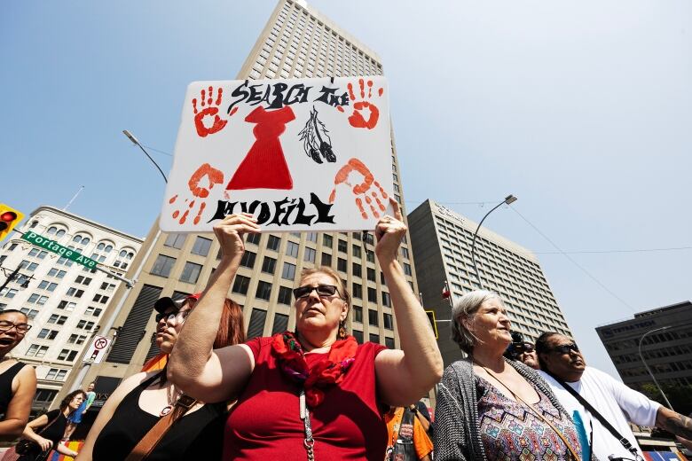 With other people standing around her, a woman holds up a sign that reads: Search the landfill.