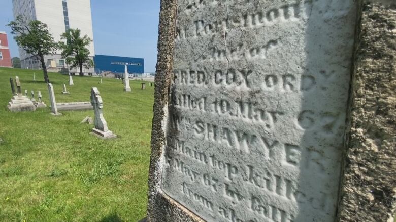 Closeup of a grave marker in white stone with other headstones and monuments in the background.