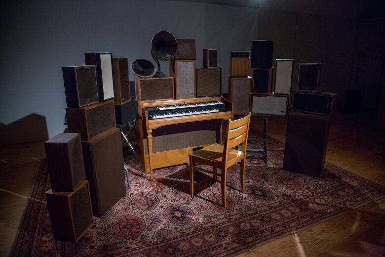 The Poetry Machine, an interactive installation by Janet Cardiff and George Bures Miller. An organ is surrounded by stacks of audio speakers. All rest on a patterned rug in a dark room.