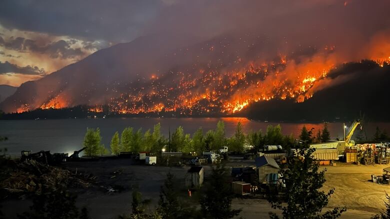 Fire and smoke climb a mountain next to businesses and homes on a lake