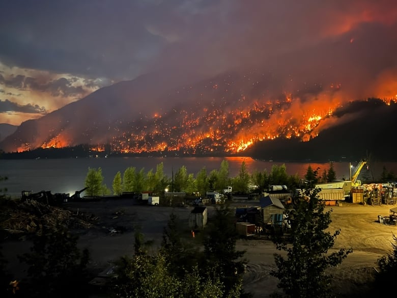 Fire and smoke climb a mountain next to businesses and homes on a lake