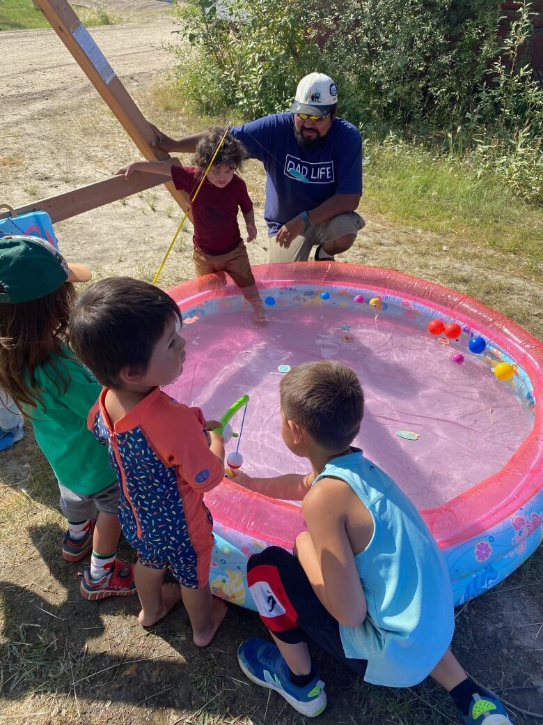 Children and a man gather around a kiddie pool, pretending to fish.