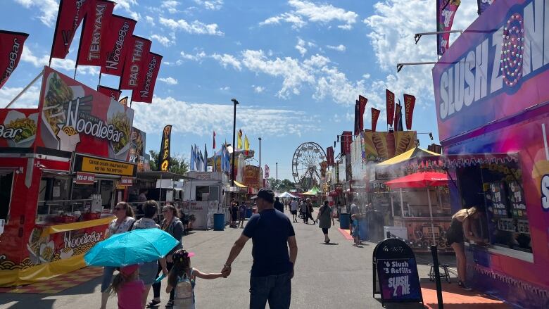 A group of people walk down the center of a long lane of food trucks