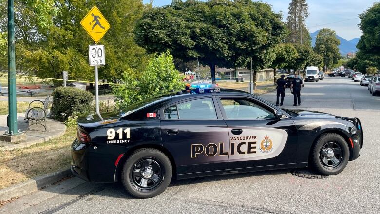 A police car is pictured next to a park which is taped off with yellow police tape.