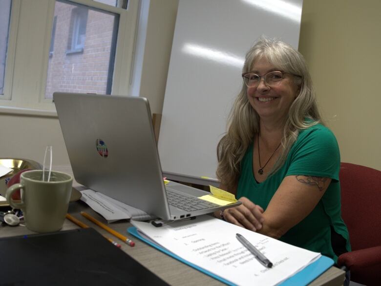 A woman sits behind a desk and smiles. 