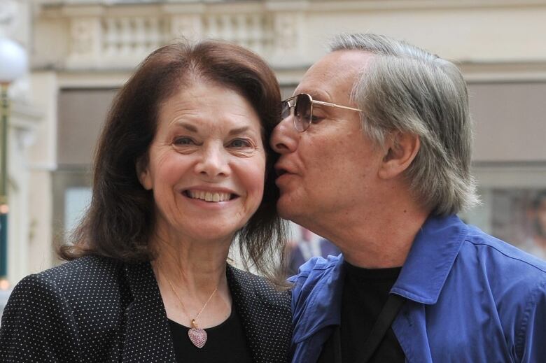 A man leans in to kiss the cheek of a smiling woman.