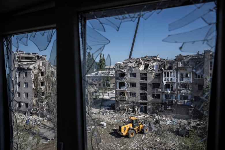 A photo taken from behind a shattered window shows workers with heavy machinery at the site of buildings destroyed during a missile strike.