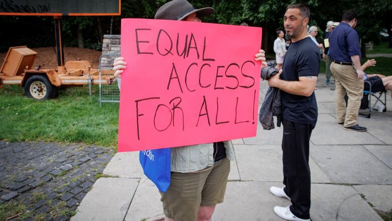 A person holding up a sign on a street corner that reads, 'Equal access for all!'