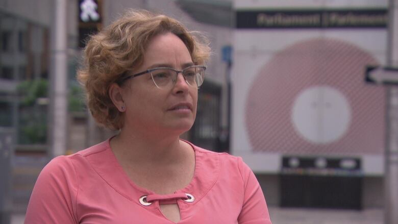 A woman stands near an intersection with a bus station in the background. 