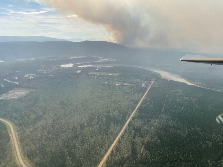 Smoke from a wildfire is seen in the distance from an airplane, with a community visible in the foreground.