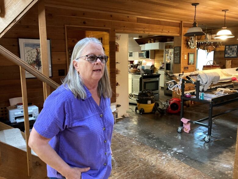 A woman stands inside a house with water on the floor.