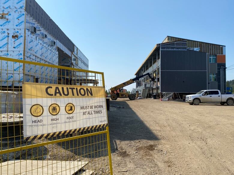 A caution sign is seen on some construction fencing with some building under construction in the background.