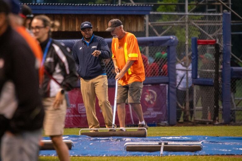 A man pushes water off a covered mound on a baseball field.