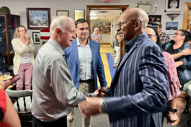 Two men shake hands in a crowded room.