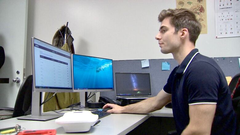 A man sits in front of computer monitors, checking the status of UV lamps that have been installed to disinfect the air. 