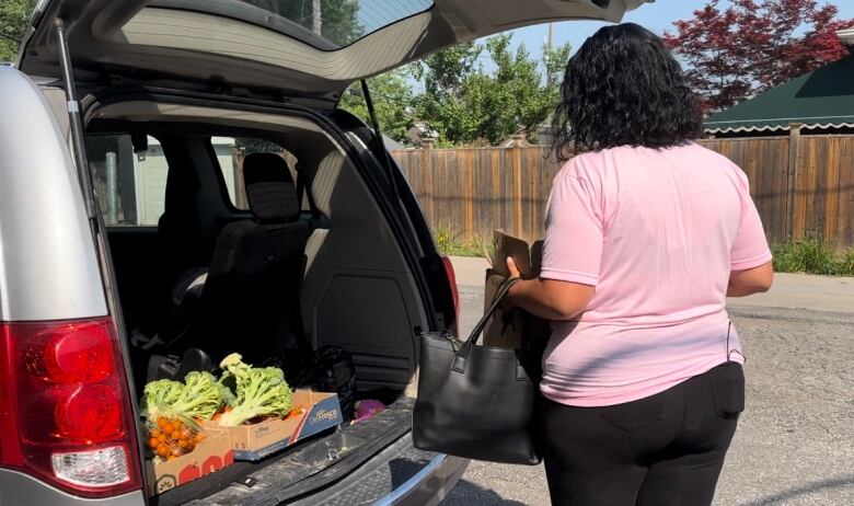 Amy Graf puts down a box of produce into her van. Inside the van are boxes of tomatoes, broccoli and bananas. 