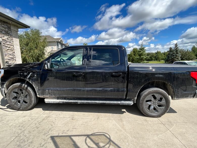 A black truck is pictured parked in a driveway with an electric vehicle charging cord plugged into it.